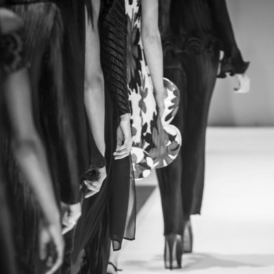 An image of models walking the runway during a fashion show, showcasing various garments in a black and white aesthetic