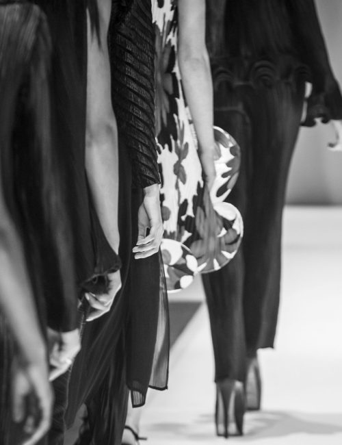 An image of models walking the runway during a fashion show, showcasing various garments in a black and white aesthetic